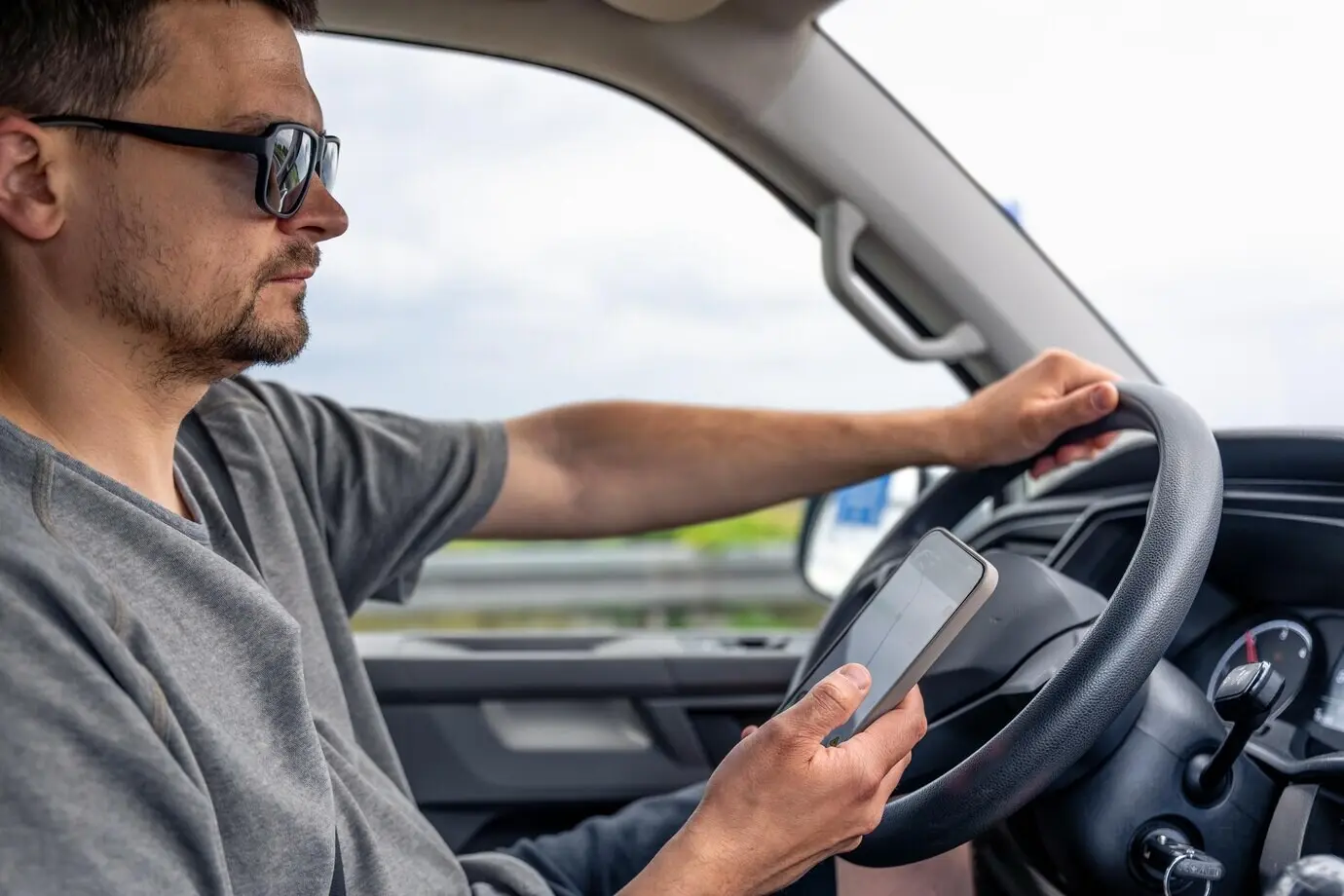 Водитель держит в руке смартфон, автомобиль движется.