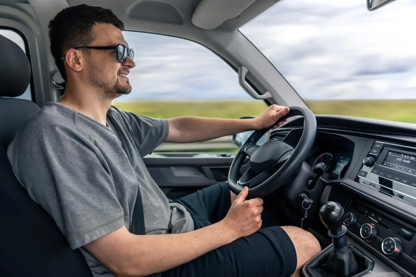 Улыбающийся мужчина за рулём автомобиля, уверенный водитель в движении, комфортное дорожное путешествие.