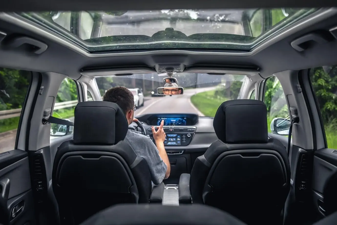 Водитель в современном автомобиле на лесной дороге жестикулирует.