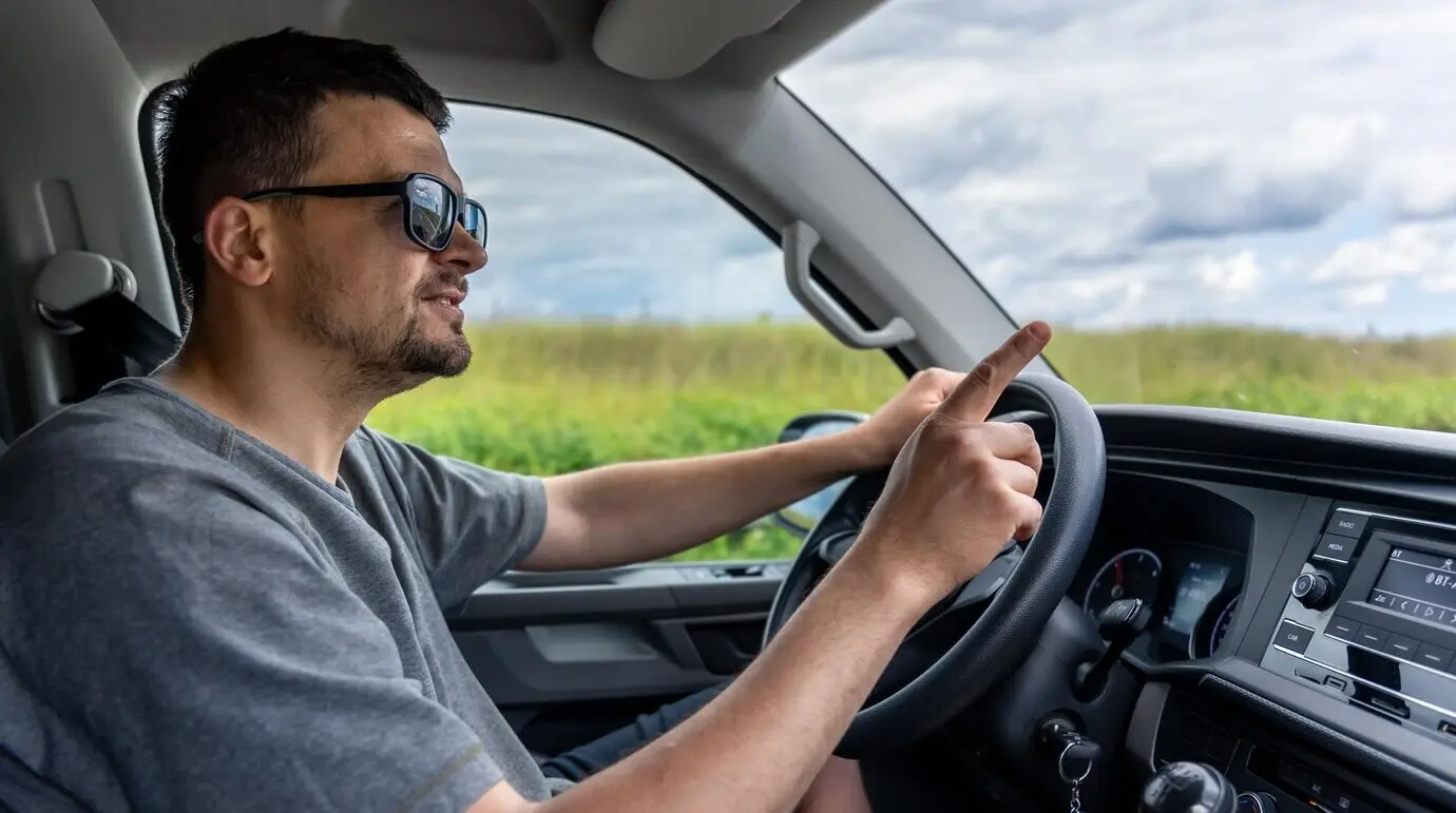 Мужчина-водитель за рулем указывает вперед; внимание сосредоточено на происходящем на дороге.